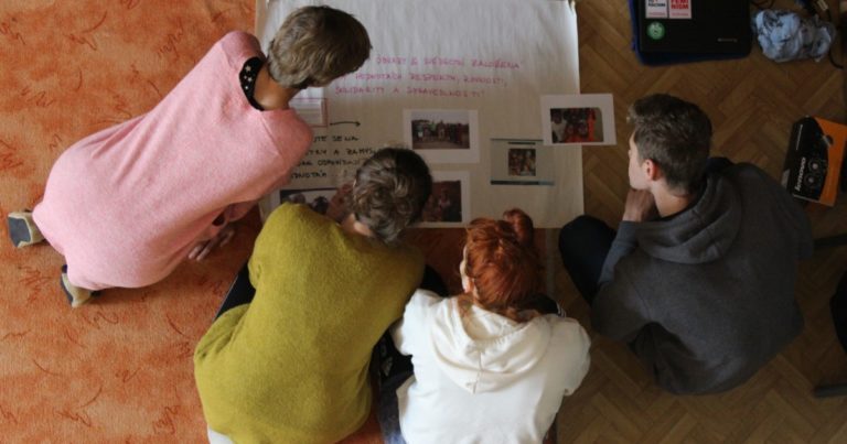 účastníci setkání si prohlíží plakát s fotkami na zemi